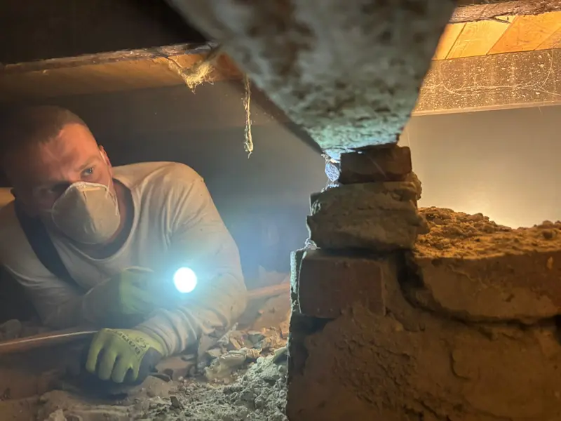 Medewerker van PuinVrij met mondkapje en zaklamp in een vervuilde kruipruimte